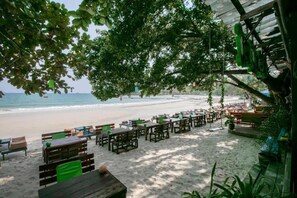 A beachside restaurant with outdoor seating, a view of the ocean, and a shaded area under trees. - Greenplace-Samed Seahorse (Rayong)