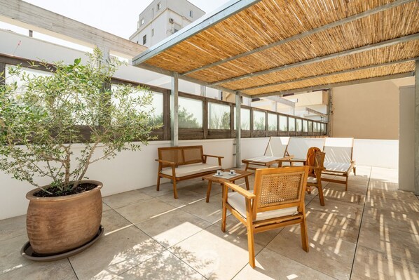 Une terrasse extérieure avec des meubles en bois, une grande plante en pot et une structure de toit en bambou.