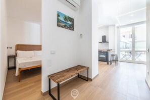 Un appartement moderne comprenant un lit, un banc, un tableau, un coin cuisine et un balcon.