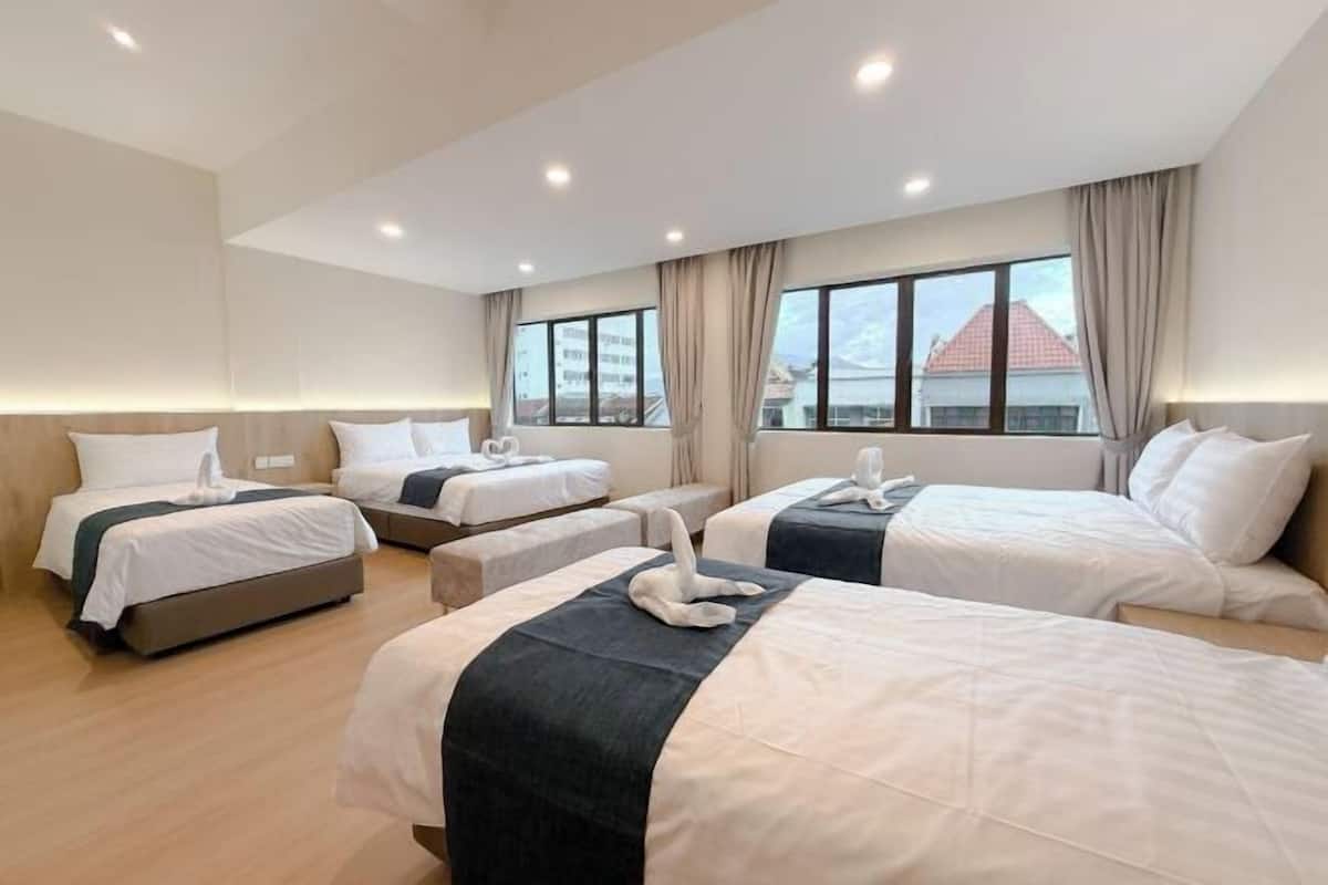 Une chambre d’hôtel avec trois lits disposés en rangée, une grande fenêtre avec des rideaux et une vue sur les bâtiments environnants.