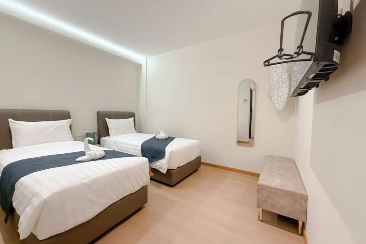Une chambre d’hôtel avec deux lits, une petite banquette, un téléviseur fixé au mur et un porte-serviettes avec des serviettes.