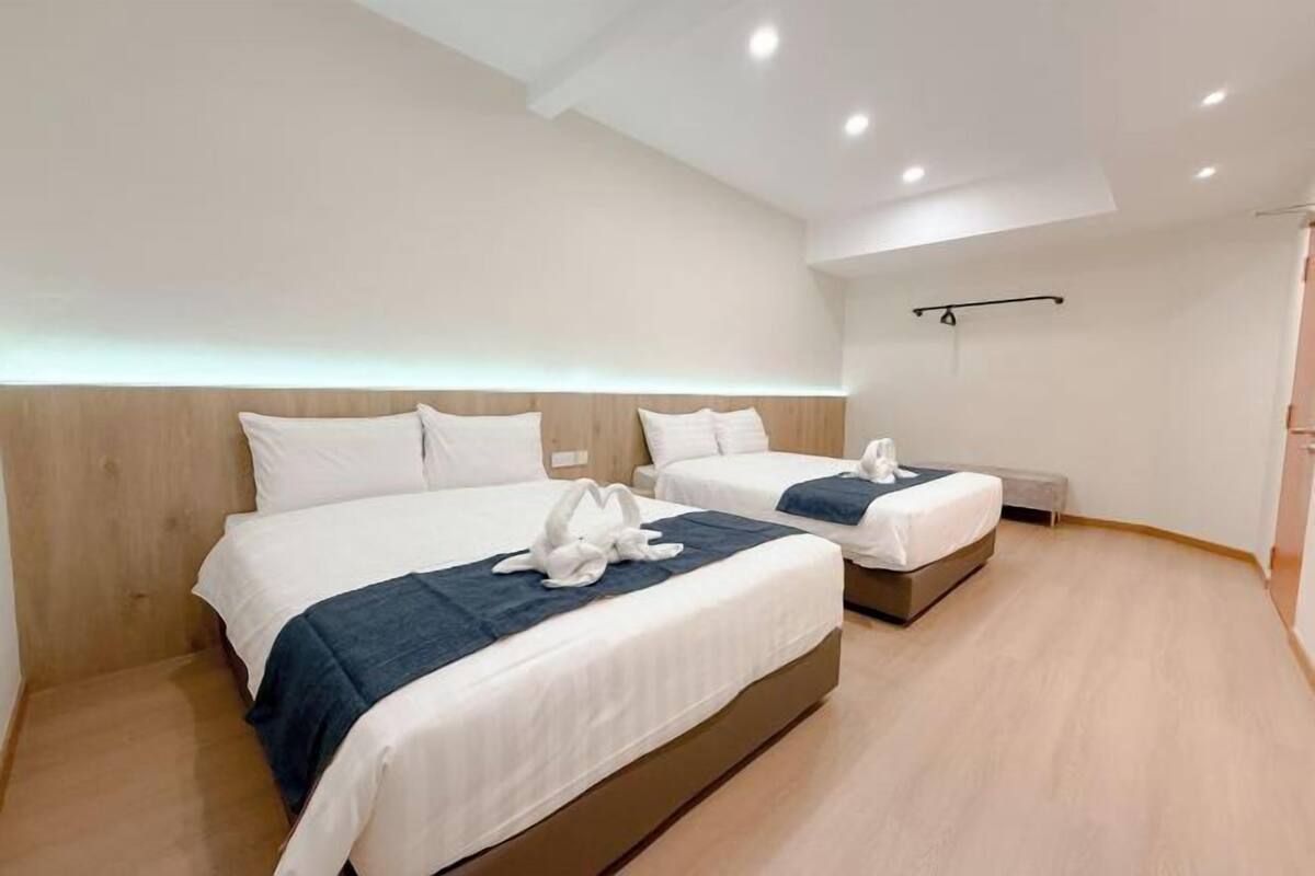 Une chambre d’hôtel avec deux lits, une tête de lit en bois, un banc et un porte-serviettes noir.