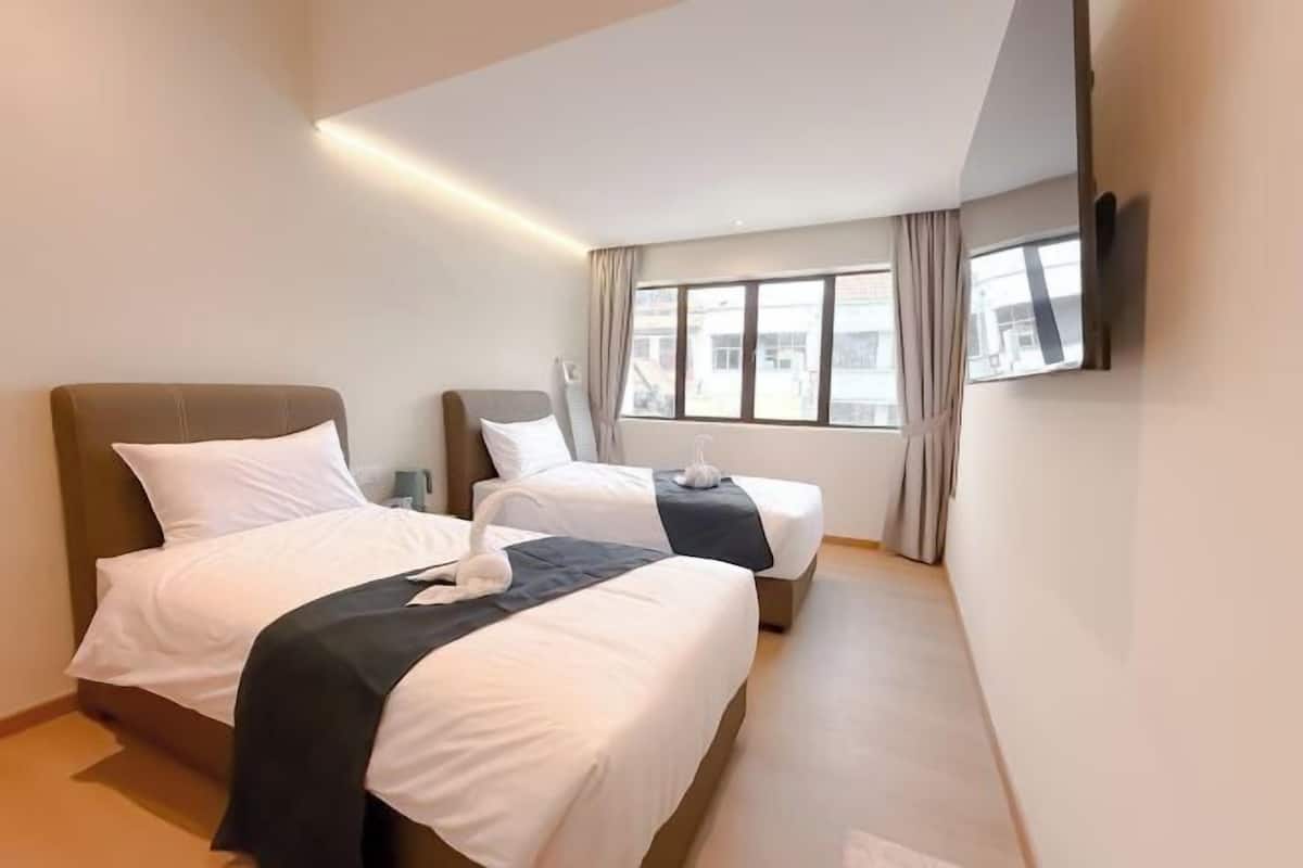 Une chambre d’hôtel avec deux lits, un téléviseur à écran plat fixé au mur et une grande fenêtre avec des rideaux.