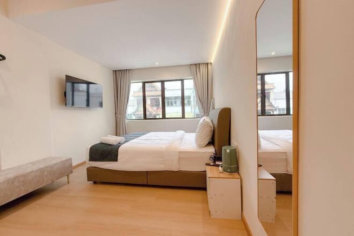 Une chambre d’hôtel moderne, équipée d’un lit, d’une table de chevet et d’un grand miroir.