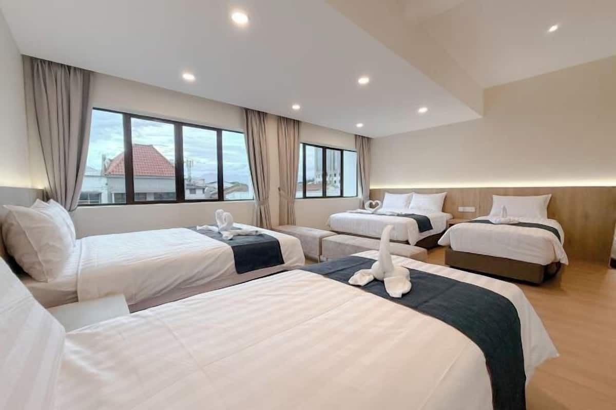 Une chambre d’hôtel avec trois lits, de grandes fenêtres et une vue sur le paysage urbain.