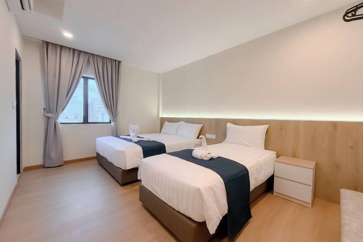 Une chambre d’hôtel moderne avec deux lits, une tête de lit en bois, une table de chevet et une fenêtre avec des rideaux.