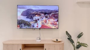 A flat-screen TV mounted on a wall, a wooden cabinet with open shelves, and a potted plant. - Resandau Stay Ipoh - Nearby Ipoh Town - Private Car Park and Lift - Whole Unit & Coliving (Ipoh)