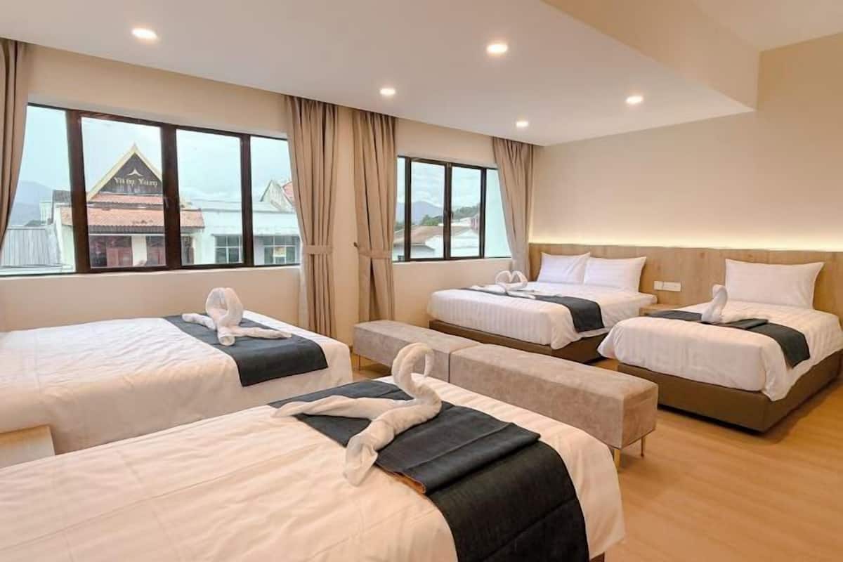 Une chambre d’hôtel avec quatre lits, de grandes fenêtres et une vue sur un bâtiment situé à l’extérieur.