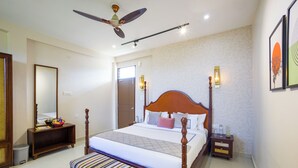 Quarto de hotel com uma cama grande, ventoinha no teto, mesa de cabeceira com abajur e um banco.