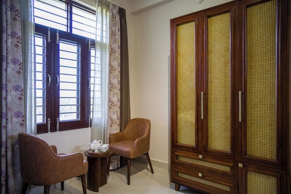 A room with a wooden wardrobe, two chairs, a small table with a teapot, and a window with curtains. - Elivaas Esh Cottage Willow | Hillside With Lush Garden (Palampur)
