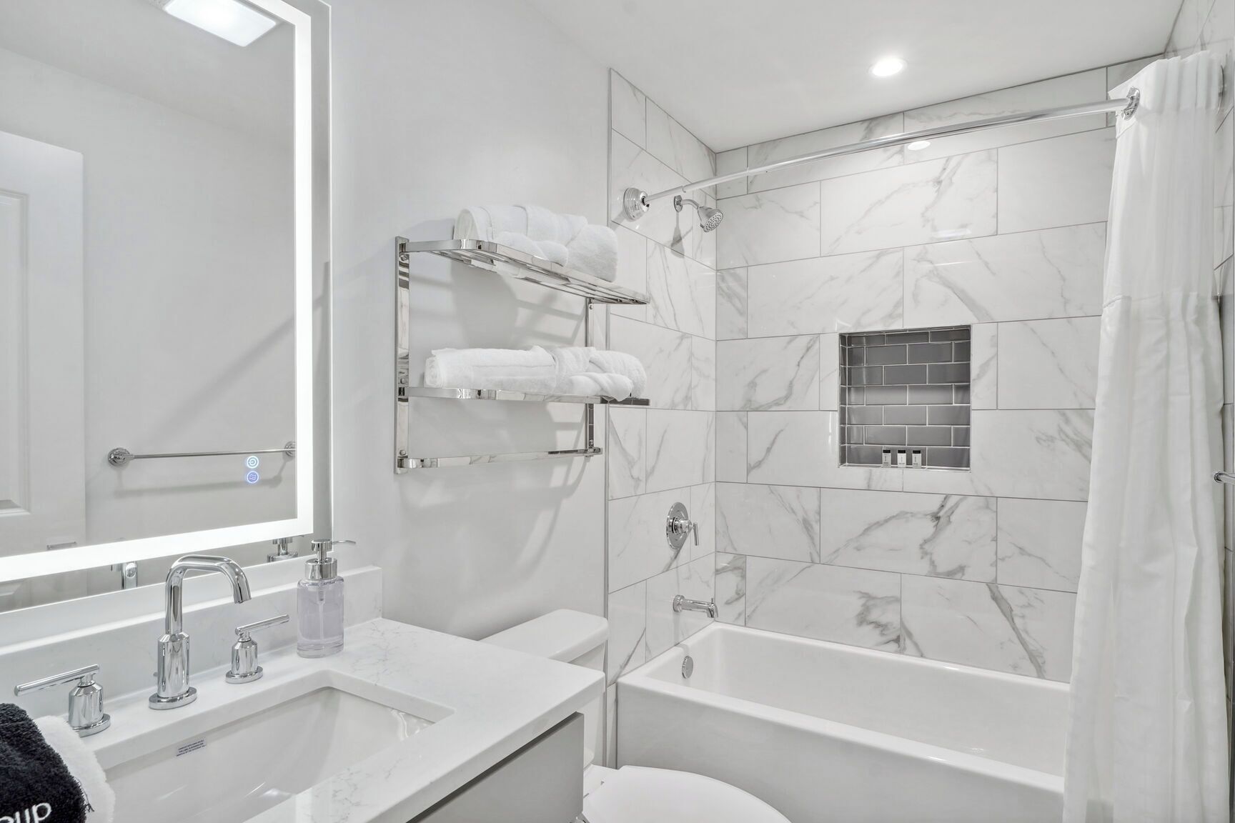 A modern bathroom with a large mirror, a bathtub, and a shower. There are multiple towel racks and a glass shower enclosure.