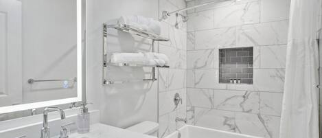 A modern bathroom with a large mirror, a bathtub, and a shower. There are multiple towel racks and a glass shower enclosure.