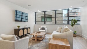 Un salon moderne doté d’une grande fenêtre, d’un téléviseur à écran plat, d’une table basse en bois et de deux canapés.