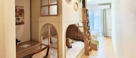 A bunk bed room with a desk and chair, a ladder, and a window with curtains.