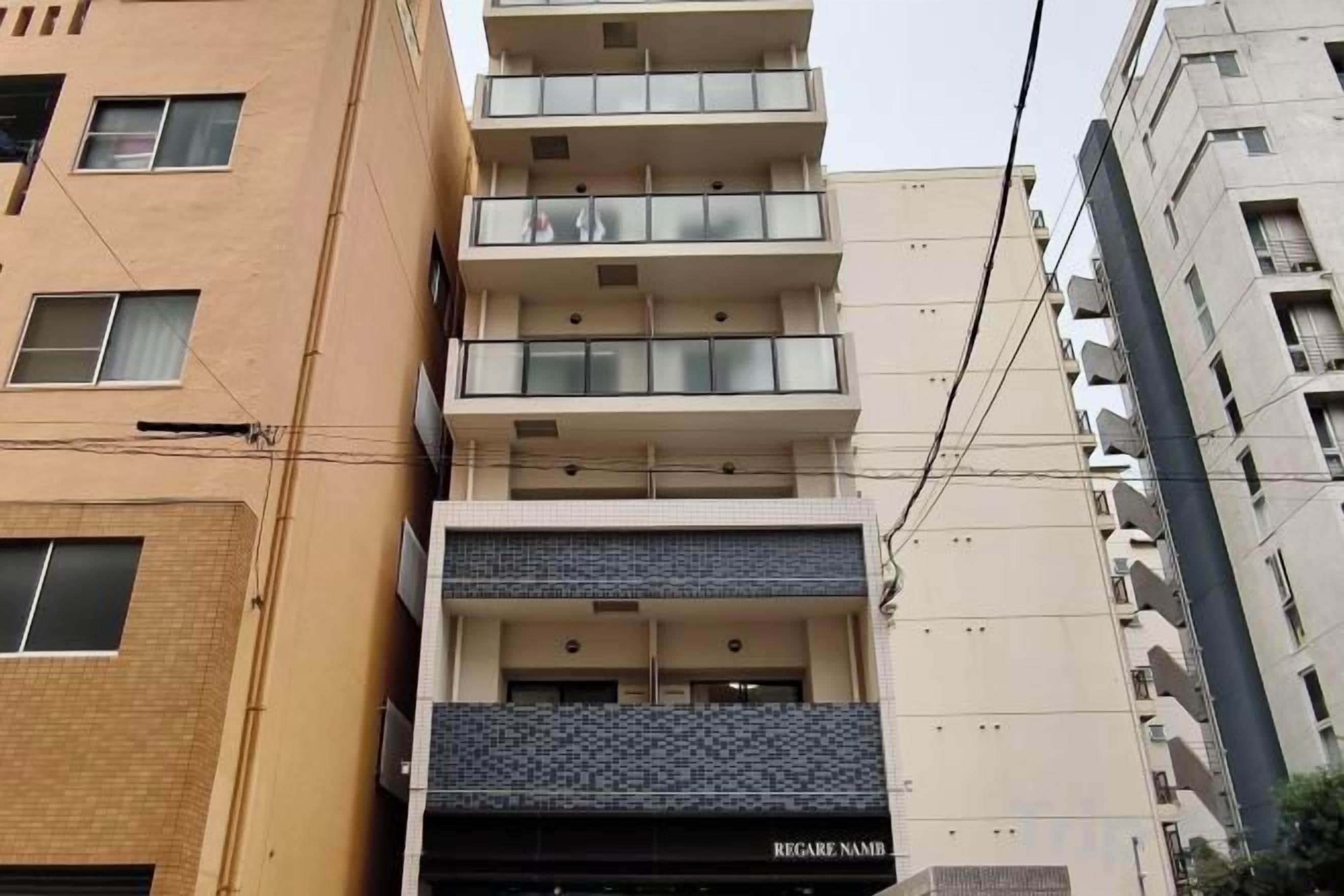 A multi-story building with a ground floor entrance, balconies on the upper floors, and a visible sign for 'REGARDE NAMB'.