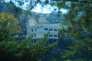 A multi-story building with a flat roof, surrounded by trees and hills.