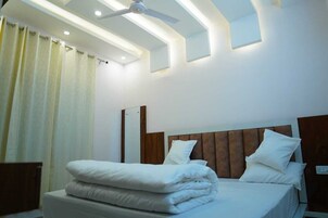 A modern hotel room with a neatly made bed, a ceiling fan, and recessed lighting.