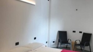 A room with a bed, a red blanket, and two black chairs.