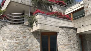 A modern building with a stone facade, balconies with red flowers, and a wooden door.