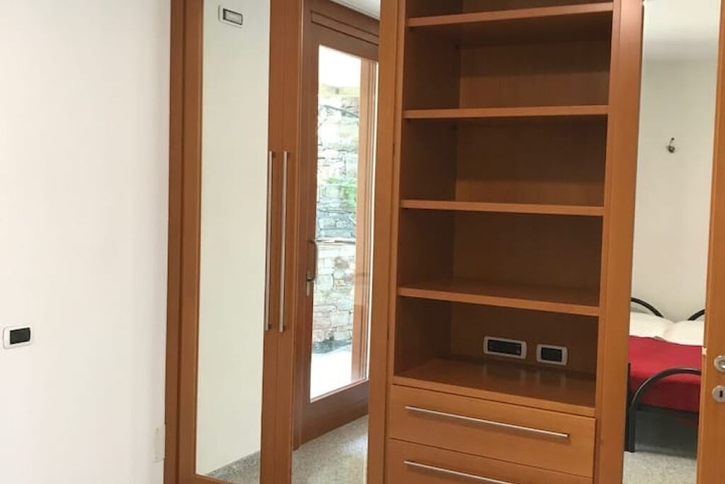 A wooden wardrobe with multiple shelves and drawers, a small window, and a door leading to a stone wall outside.