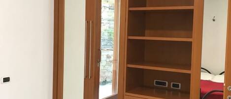 A wooden wardrobe with multiple shelves and drawers, a small window, and a door leading to a stone wall outside.