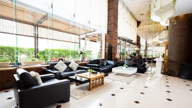 Eine großzügige Lobby mit schwarzen Ledersofas, einem Holztisch und einem großen Glassfenster mit Blick ins Grüne.
