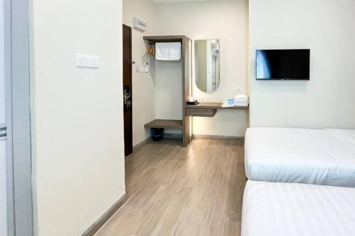 A hotel room with a bed, a TV, a mirror, and a small bathroom area.