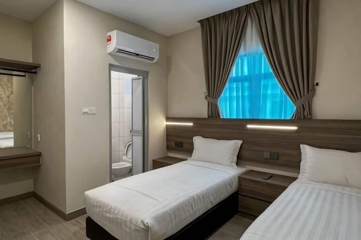 A hotel room with two beds, an air conditioning unit, a window with curtains, and a shower area.