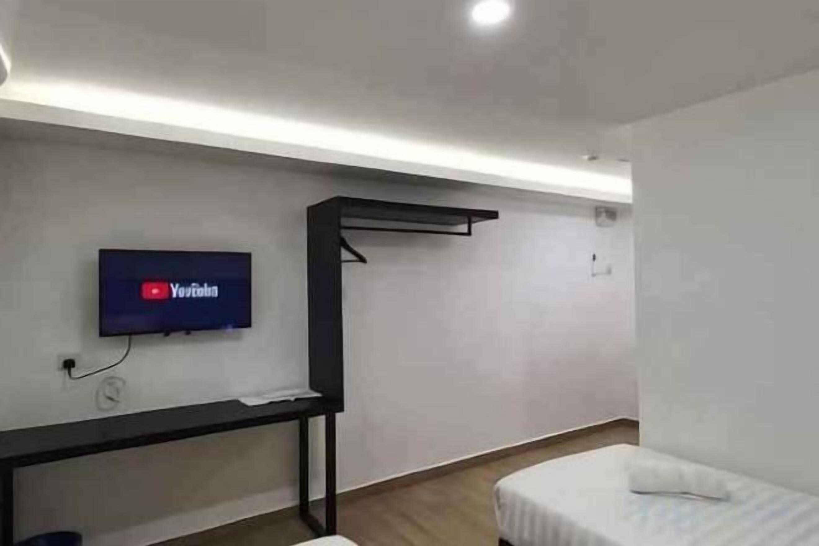 A hotel room with a bed, a TV mounted on the wall, a desk, and a hanging storage unit.