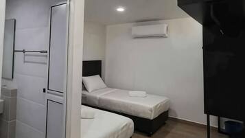 Una habitación pequeña y compacta con dos camas, una puerta blanca y una estructura negra a la derecha.