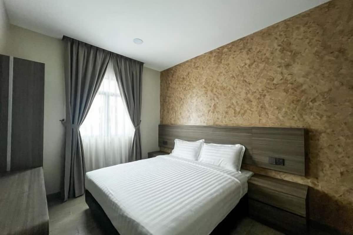 A hotel room with a large bed, a wooden headboard, a nightstand, and a window with curtains.