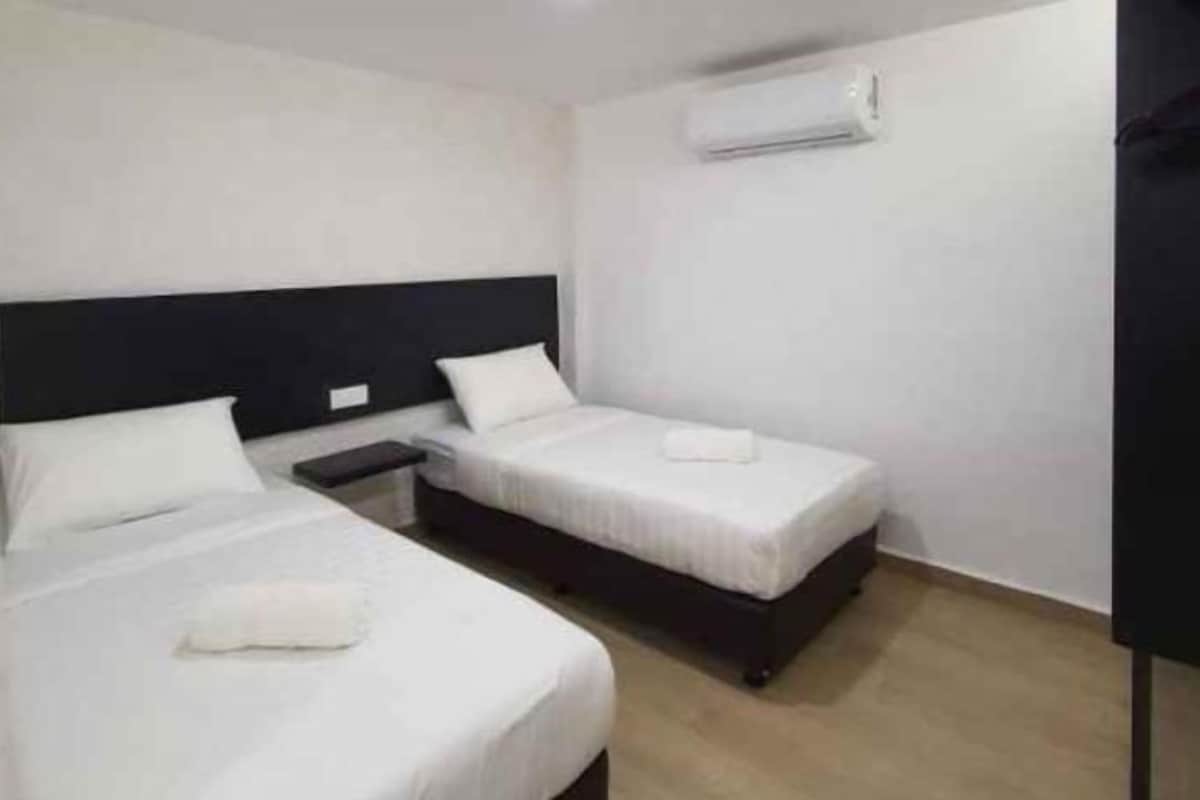 Une chambre d’hôtel avec deux lits simples, une table de chevet et un climatiseur fixé au mur.