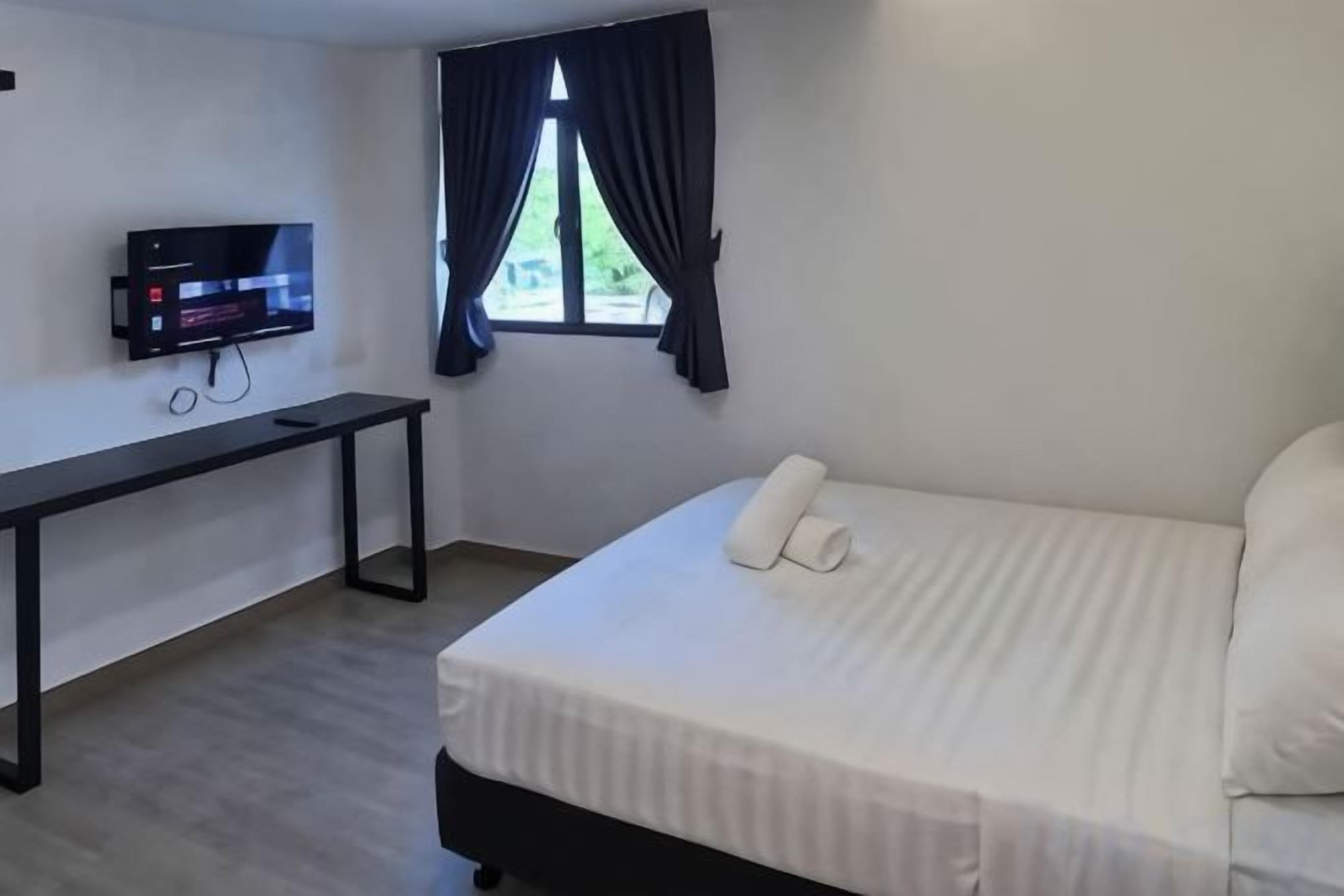 Habitación de hotel con cama, escritorio, televisor y ventana con cortinas.