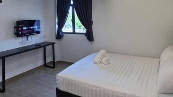 Habitación de hotel con cama, escritorio, televisor y ventana con cortinas.
