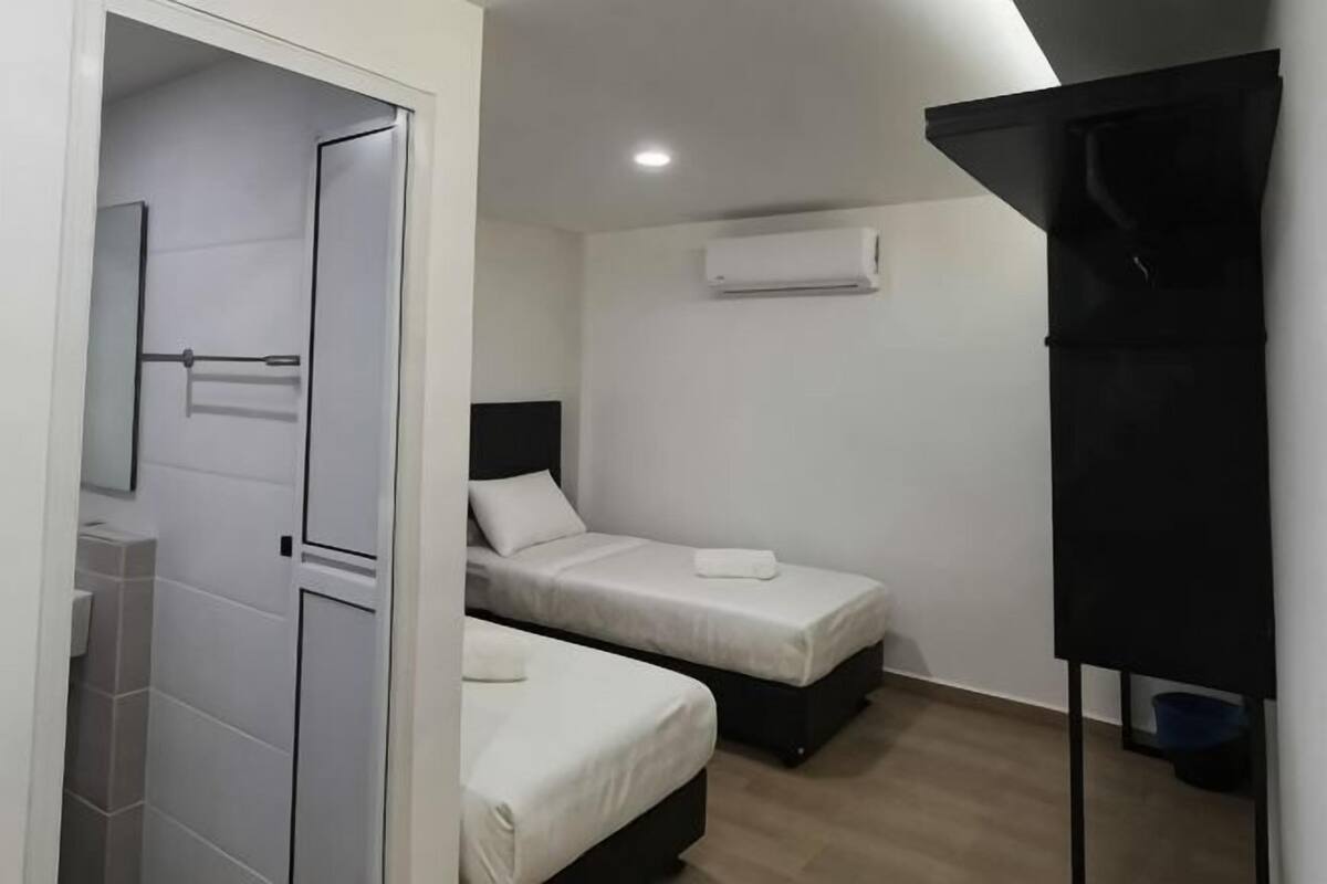 A small, modern room with two beds, a shower, and a black storage unit.