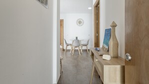 Ein Flur, der in einen Essbereich führt, mit einem runden Tisch und Stühlen, einer Uhr an der Wand und einer Holztür.