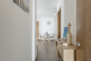 A hallway leading to a dining area with a round table and chairs, a clock on the wall, and a wooden door.