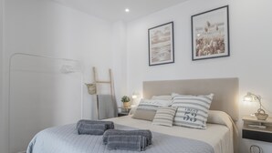 Ein Schlafzimmer mit einem Bett, Kissen, einem Nachttisch, einer Lampe, einem Spiegel und einem Wandbild.