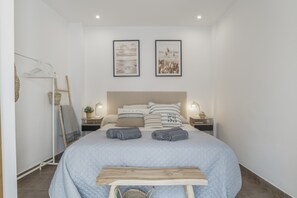 A bedroom with a bed, two wall-mounted pictures, a bedside table with a lamp, and a wooden bench.