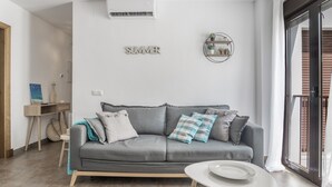 Ein modernes Wohnzimmer mit einem grauen Sofa, einem kleinen weißen Tisch und einer Wandablage mit Pflanzen.