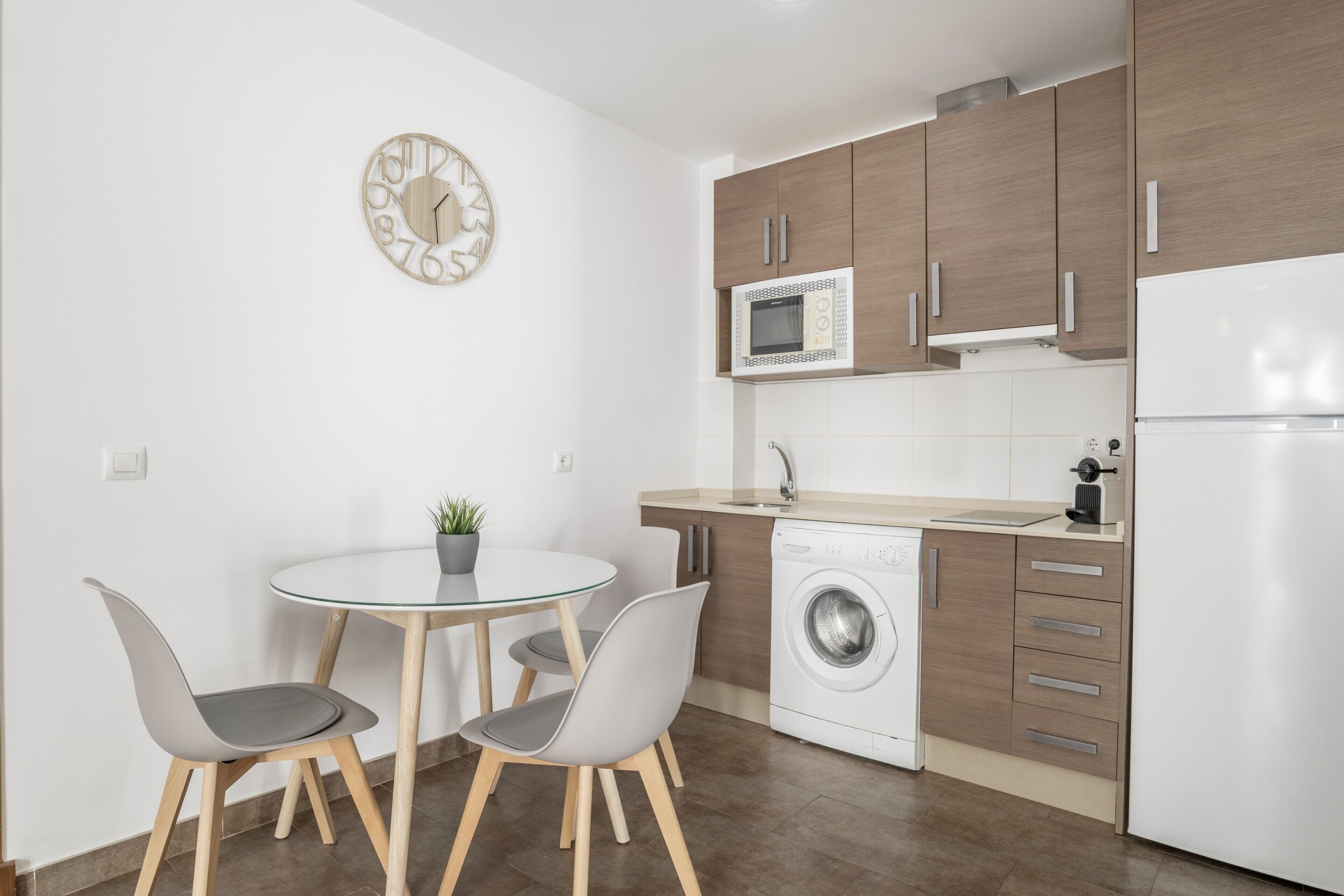 Una cocina compacta con microondas, lavadora y zona de comedor con sillas y mesa.