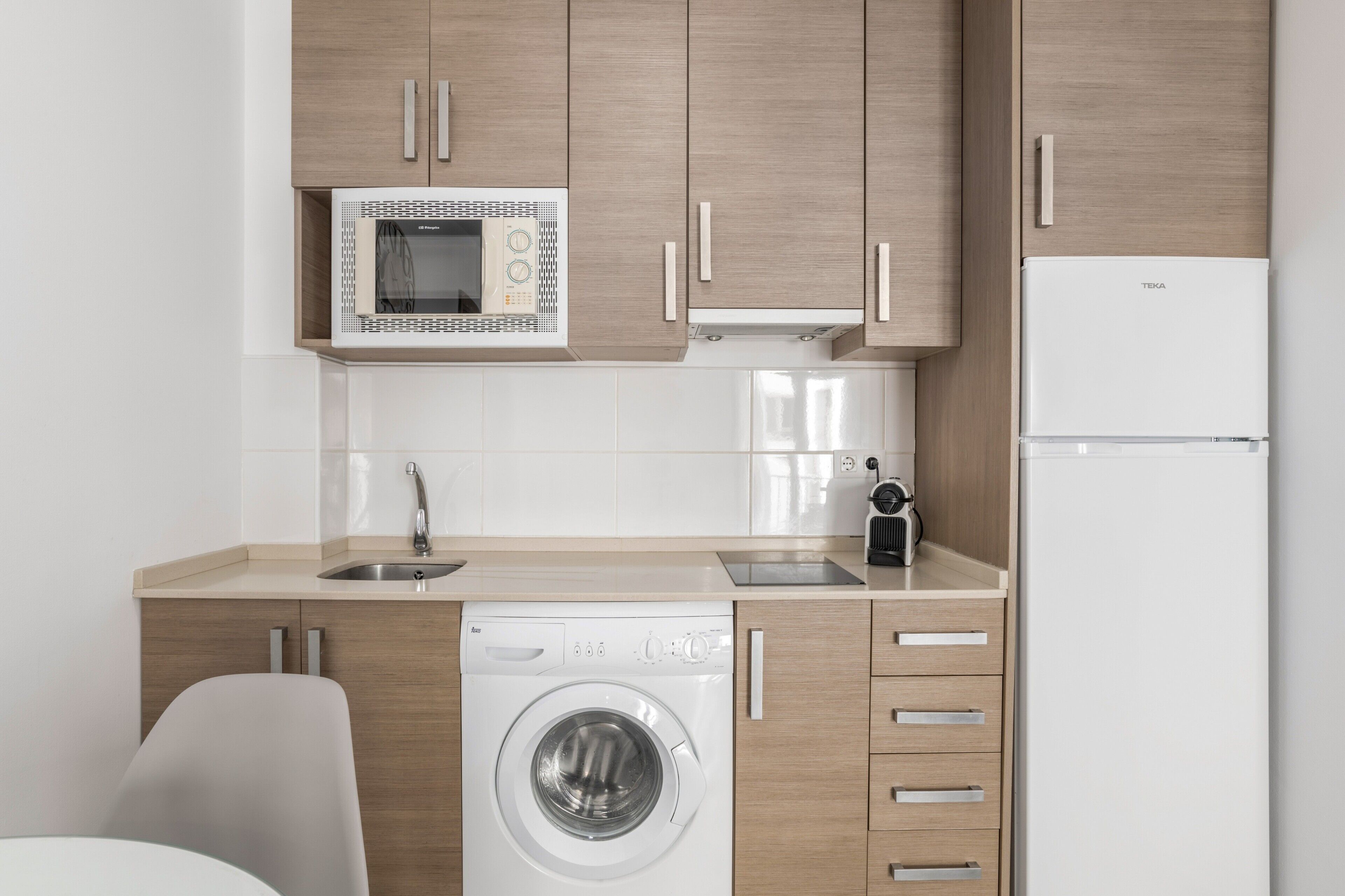 A modern kitchen with wooden cabinets, a built-in microwave, a washing machine, and a refrigerator.