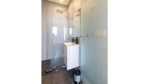 Un baño moderno con cabina de ducha de vidrio, un lavamanos blanco y un cubo de basura.