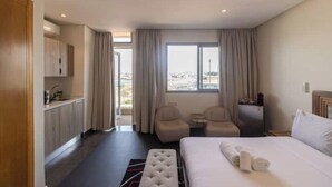 Habitación de hotel con cama, dos sillones, una mesita, un minibar y vistas al exterior.