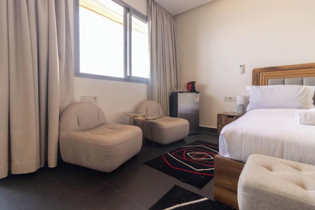 Une chambre d’hôtel avec un lit, deux fauteuils, une petite table et une table de chevet.