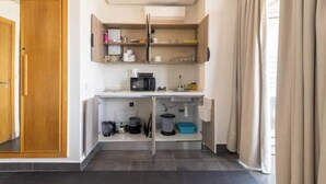 Cocina compacta con microondas, cafetera y estantes para guardar objetos.