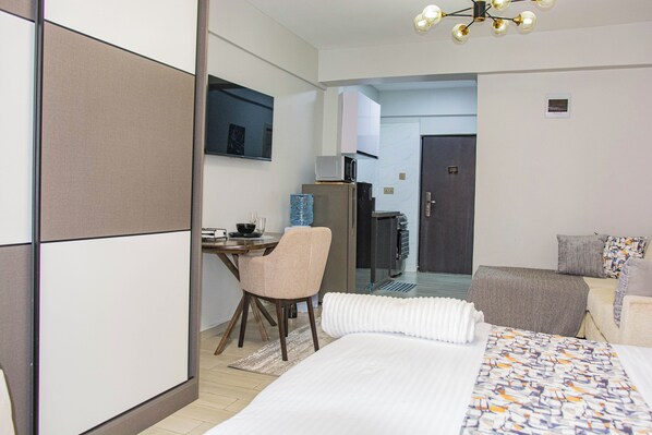 A hotel room with a bed, a desk, a chair, a microwave, a refrigerator, and a water dispenser.