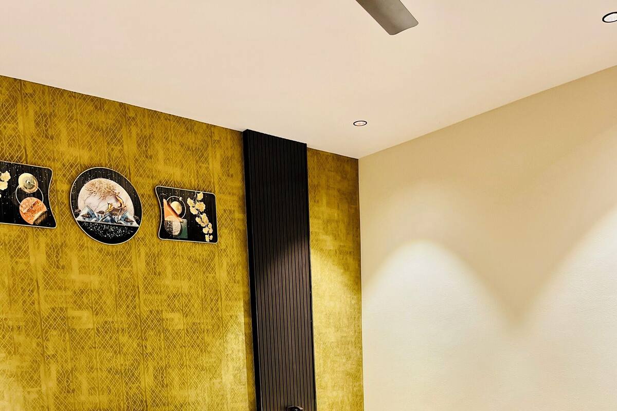A hotel room with a bed, pillows, a headboard, a wall with pictures, and a small table with flowers.