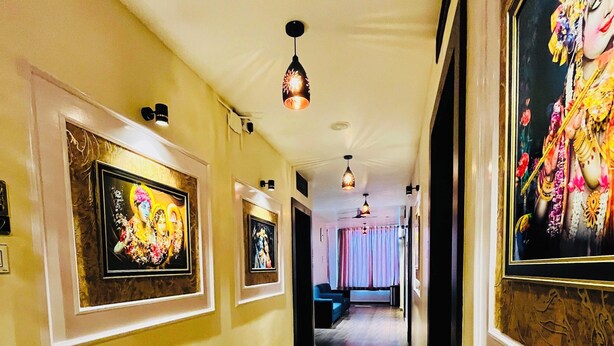 A hallway with framed artwork on the walls, a wooden floor, and a ceiling fan. - Shubh Laxmi Residence (Ajmer)