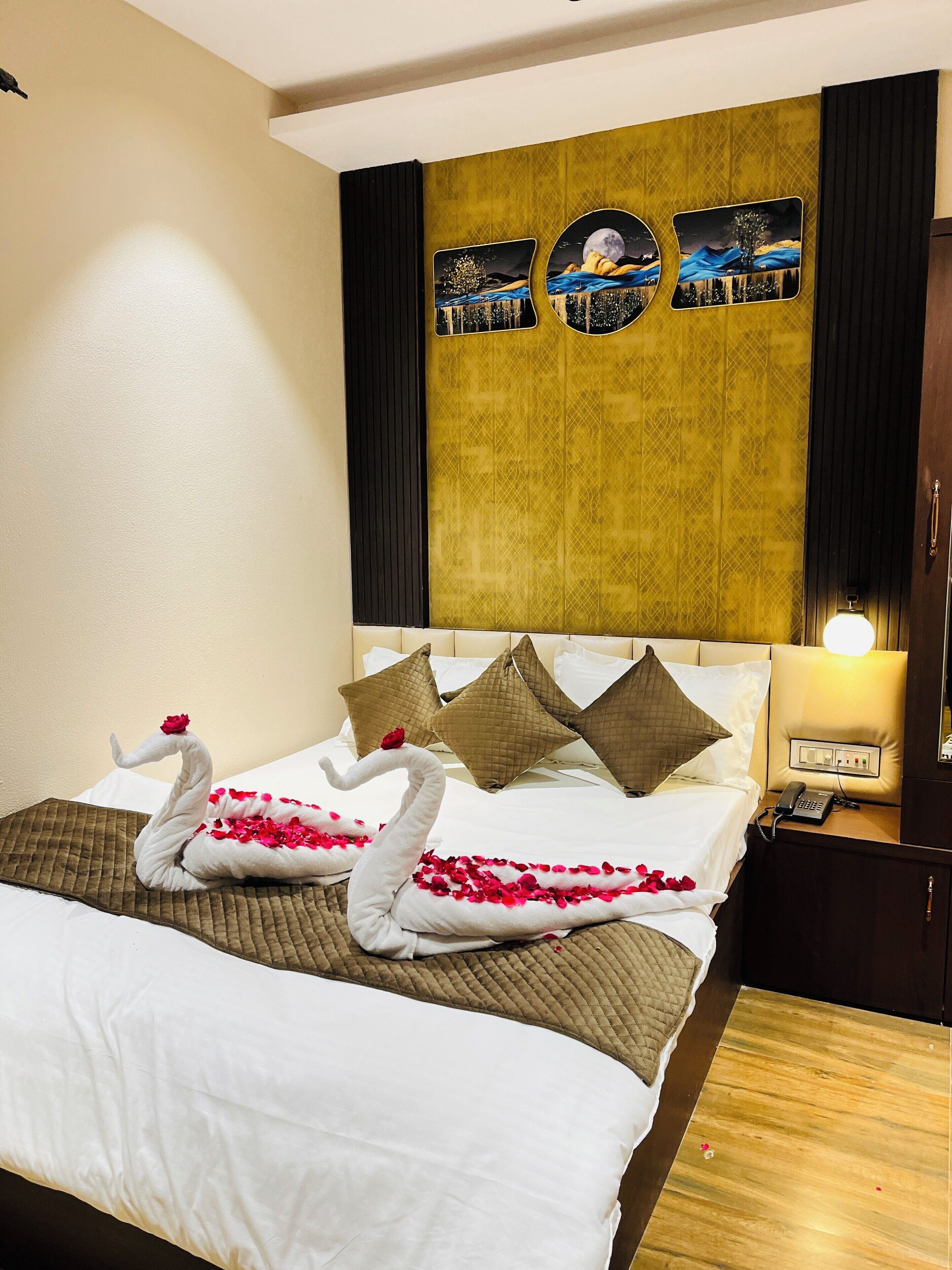 A hotel room with a bed, decorative pillows, a wall with artwork, a bedside table with a lamp, and a phone.